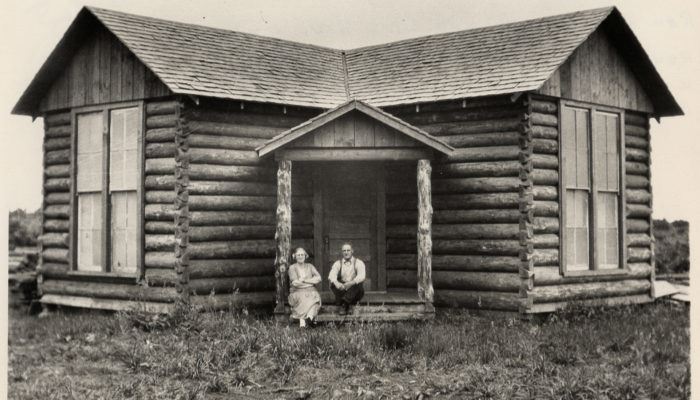 Old Photo of Two People Sitting on the Steps of the Little Log Church